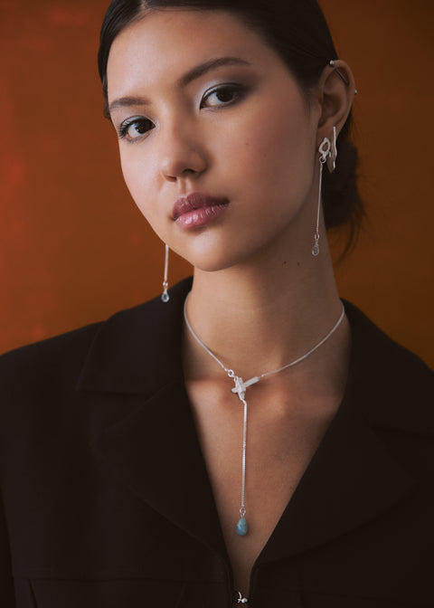 Woman wearing a necklace and earrings against an orange background