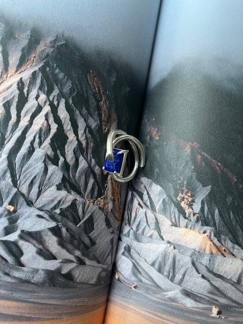A Lapis Lazuli ring with a silver band, showcased on a textured background.