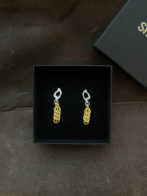 Pair of gold chain earrings in a black box on a dark textured surface.