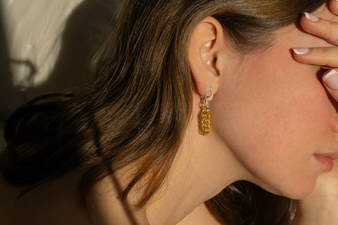 Close-up of a woman wearing gold chain earrings with a blurred background