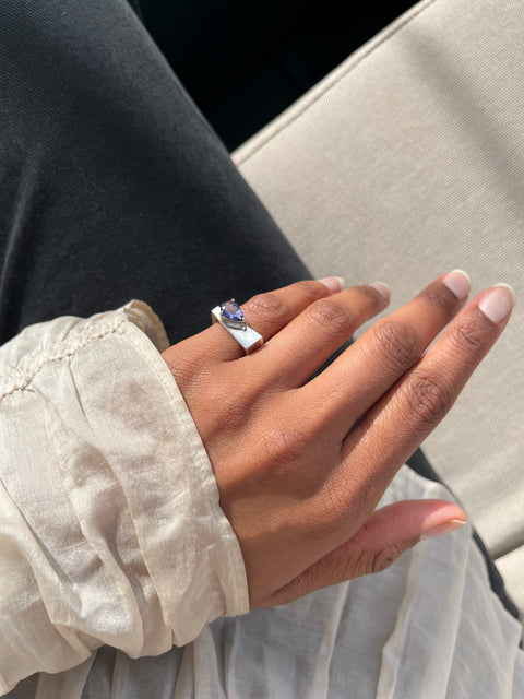 Hand wearing a ring with a blue gemstone against a neutral background