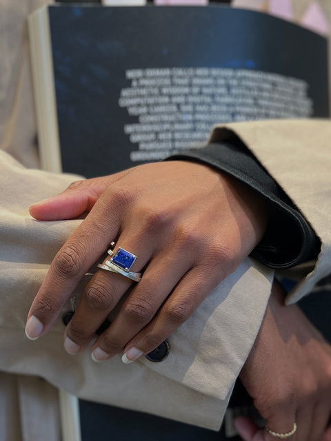 Close-up of a hand wearing a ring with a blue stone, holding a book.