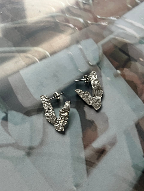 A pair of silver 925 earrings with a textured surface, displayed on a reflective surface.